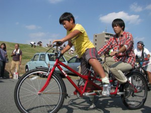 （写真）タンデム自転車の前に子どもが、後ろに大学生が乗っている