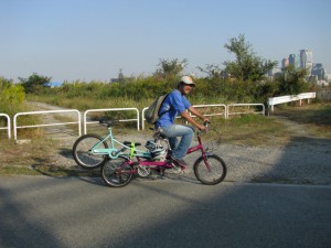（写真）普通のタンデム自転車に車椅子に取り付けるタイプの自転車を取り付けて運んでいます。