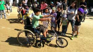 （写真）ハンドサイクルに乗った男の子の周りで子どもたちや親御さんが見守っています