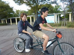 （写真）ボランティアスタッフの大学生２人がタンデム自転車に乗って、今から宣伝活動に行きます