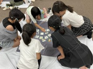 女の子が5人でかるた10枚ほどを囲む。一人が札に手をのばしている